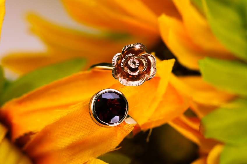 Sculpted gold rose ring with garnet, photographed among sunflower petals