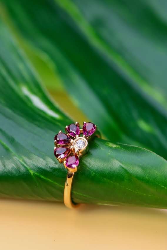 Gold ring with pink sapphire petals arranged as a blossom, on a green leaf